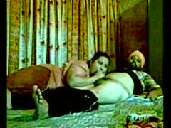 Acting on camera, a real Punjabi Sikh couple sits on an ottoman.